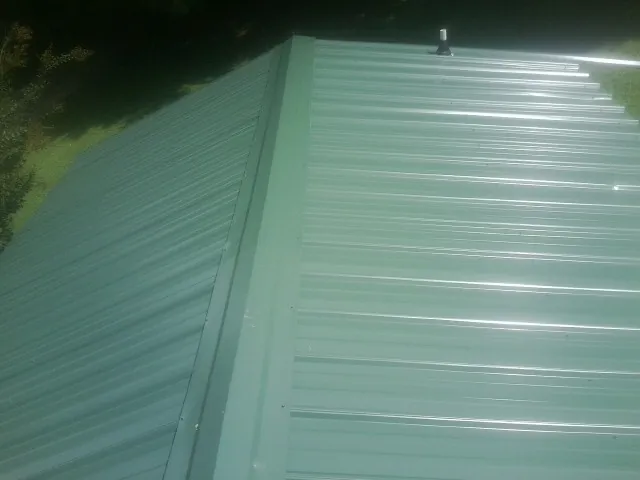 New green metal panels meeting at the ridge of a roof — Flat Roof Repair work by our crew in Bradley