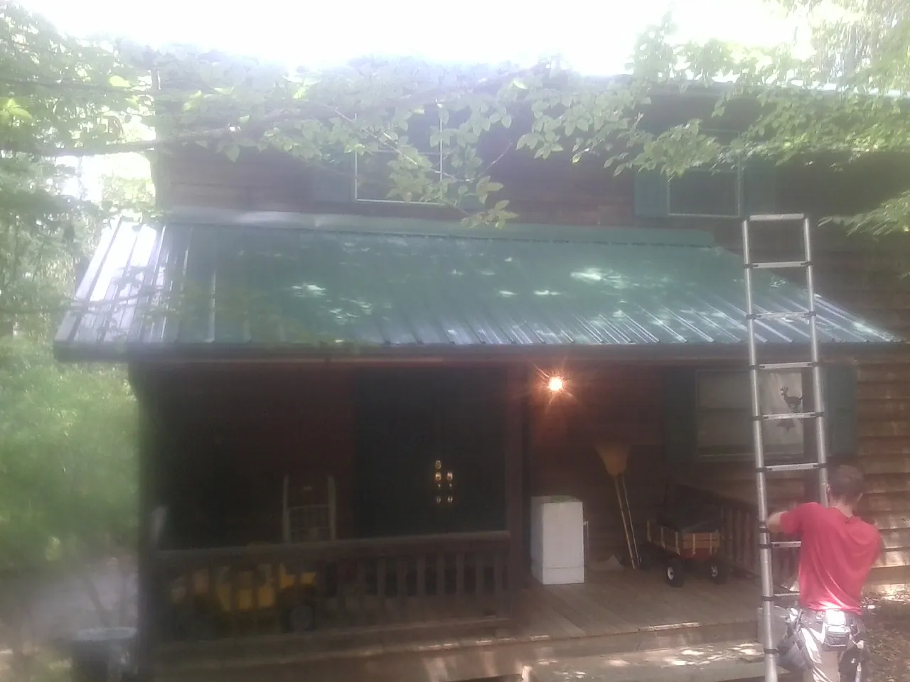 Worker on a ladder at the green porch roof of a wooded cabin in Bradley