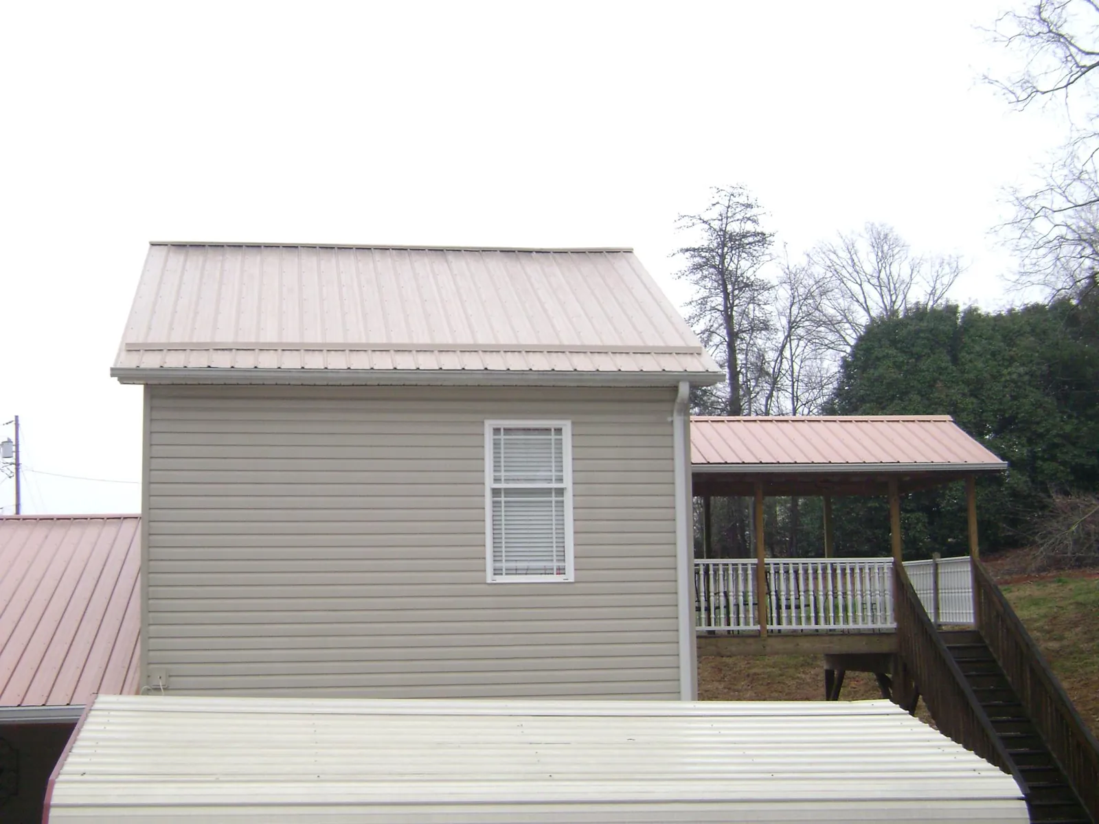 Tan metal roofs on a two story addition and attached porch, from a Roof Replacement job in Bradley